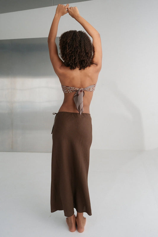Person wearing a brown skirt and topless top against a neutral background