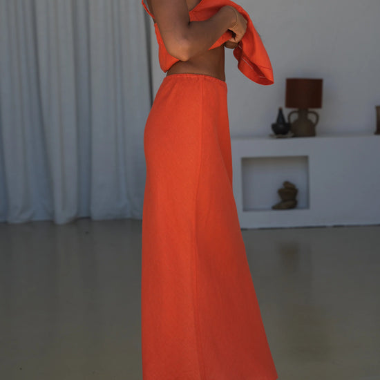 Person wearing an orange outfit standing in a minimalistic room with white curtains.