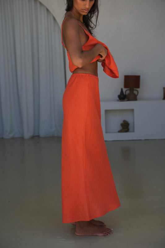 Person wearing an orange outfit standing in a minimalistic room with white curtains.