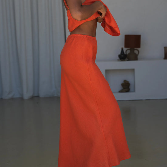 Person wearing an orange outfit standing in a minimal indoor setting.