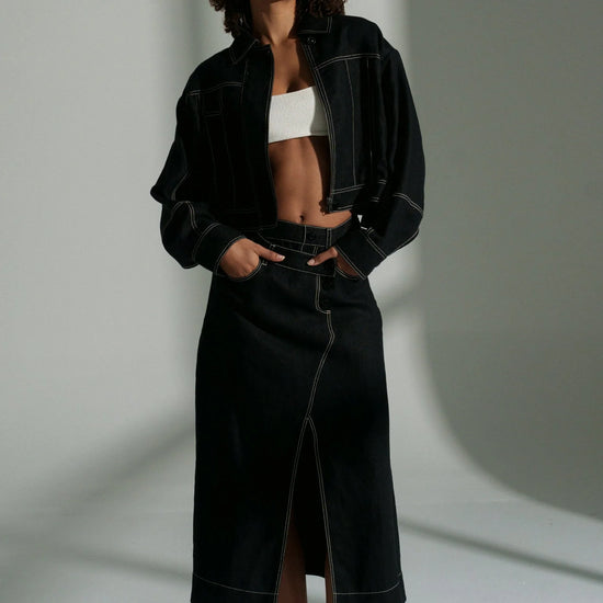 Woman wearing a black linen jacket and skirt with a white top against a neutral background