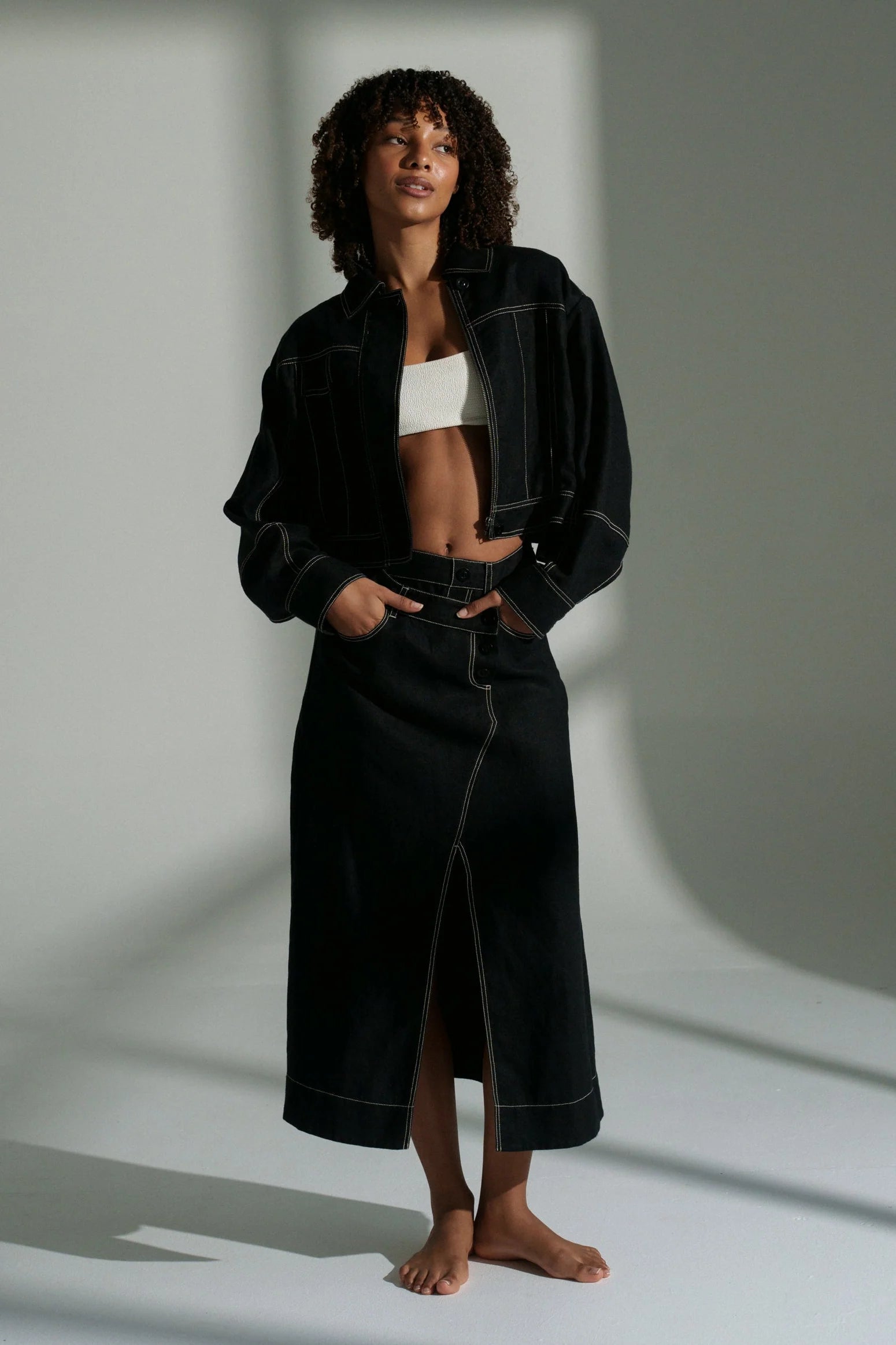 Woman wearing a black linen jacket and skirt with a white top against a neutral background