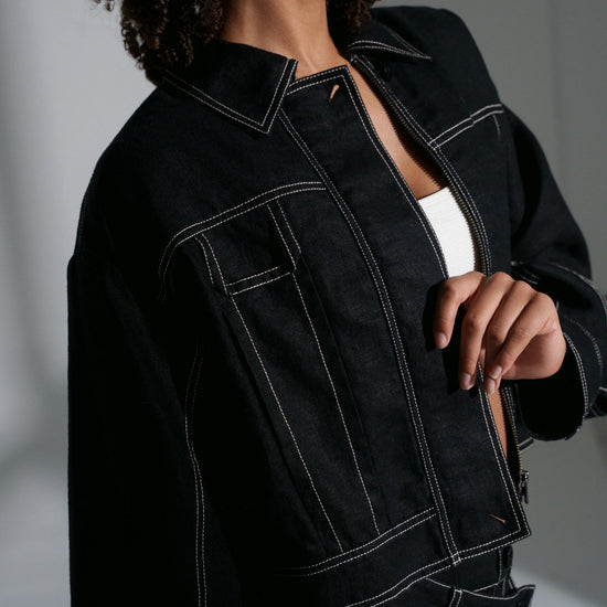 Person wearing a black linen jacket with white stitching on a neutral background