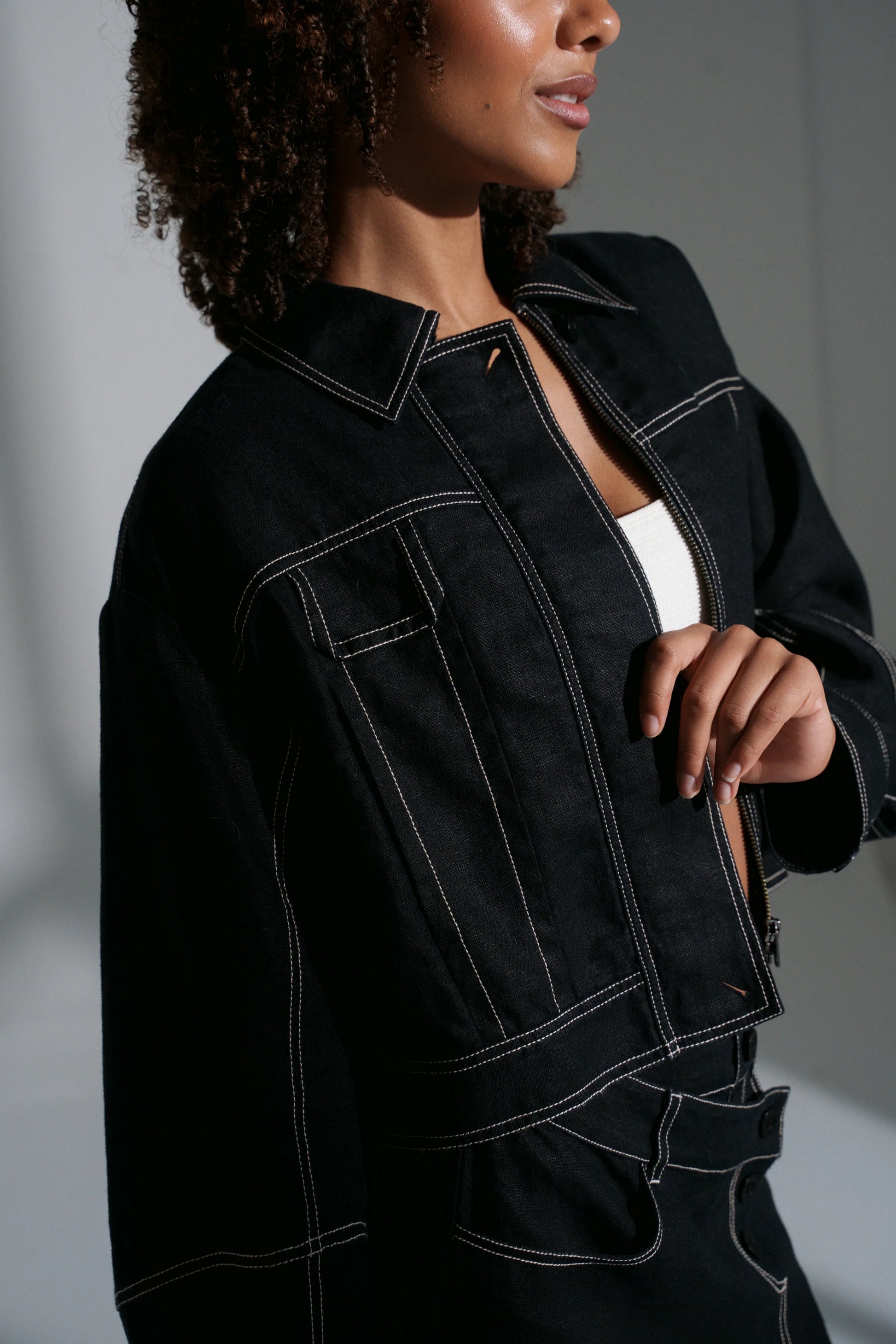 Person wearing a black linen jacket with white stitching on a neutral background