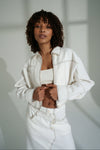 Woman wearing a white linen jacket and skirt against a neutral background
