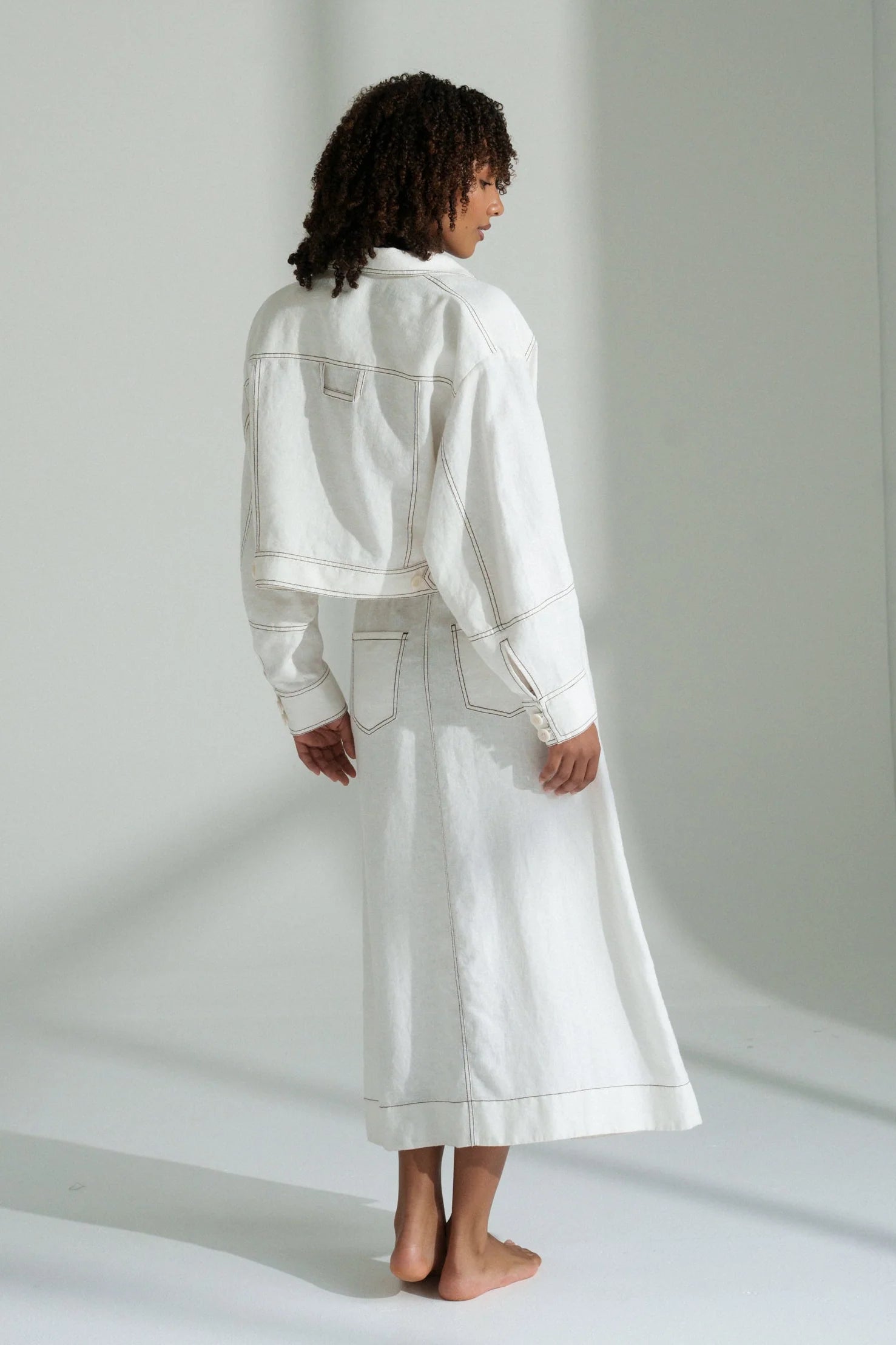 Person wearing a white linen jacket and skirt set against a plain background
