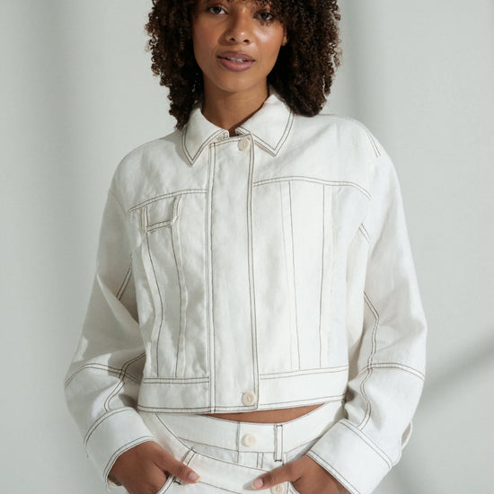 Woman wearing a white linen jacket and pants against a plain background