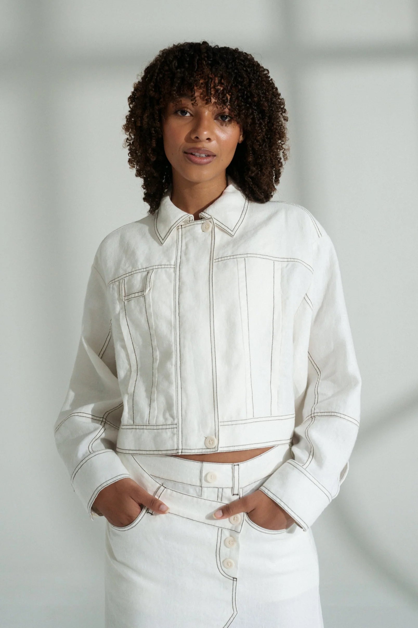 Woman wearing a white linen jacket and pants against a plain background