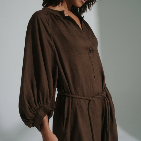Woman wearing a brown linen dress against a plain background