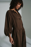 Woman wearing a brown linen dress against a plain background