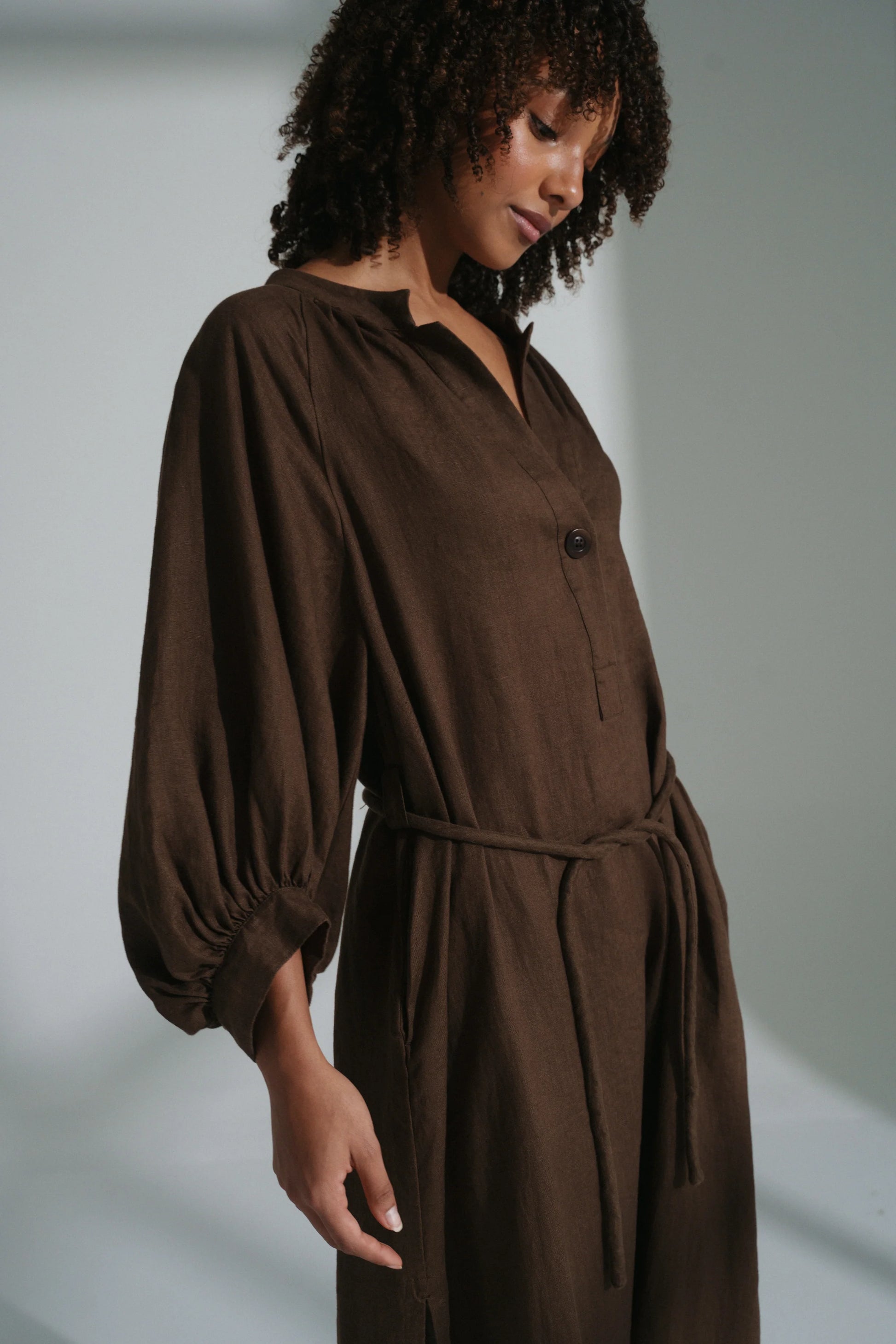 Woman wearing a brown linen dress against a plain background