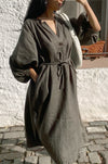 Woman wearing a long, dark green linen dress standing on a stone pavement.