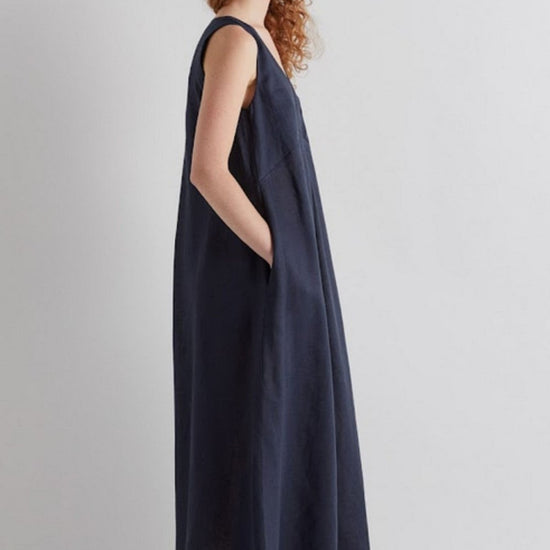 Woman wearing a dark blue sleeveless jumpsuit against a light gray background