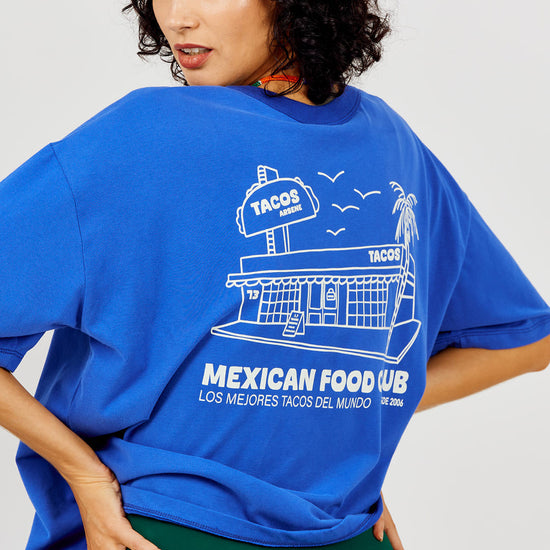 Person wearing a blue oversized t-shirt with a graphic design on a plain background