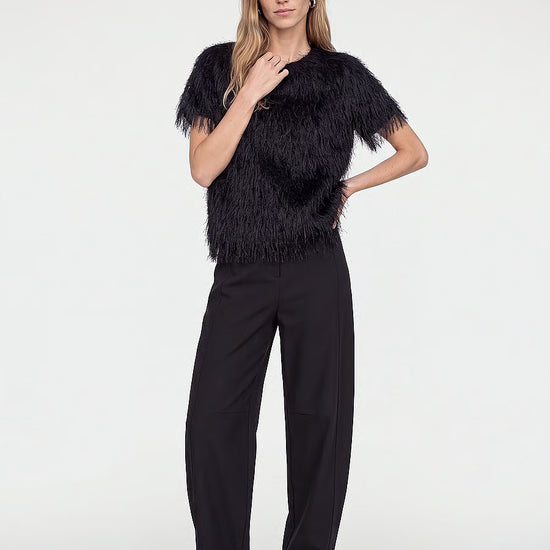 Model wearing a black feather-trimmed short-sleeve top, black wide-leg trousers, and black pointed heels.