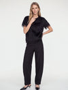 Model wearing a black feather-trimmed short-sleeve top, black wide-leg trousers, and black pointed heels.