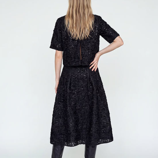 model facing away from the camera, wearing an a-line sequin skirt and matching top with black boots