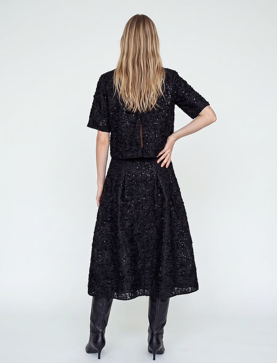 model facing away from the camera, wearing an a-line sequin skirt and matching top with black boots