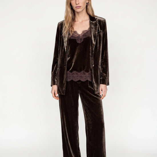 model wearing a brown velvet suit and a brown lace and velvet texture camisole with white heels ona plain grey background