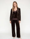 model wearing a brown velvet suit and a brown lace and velvet texture camisole with white heels ona plain grey background