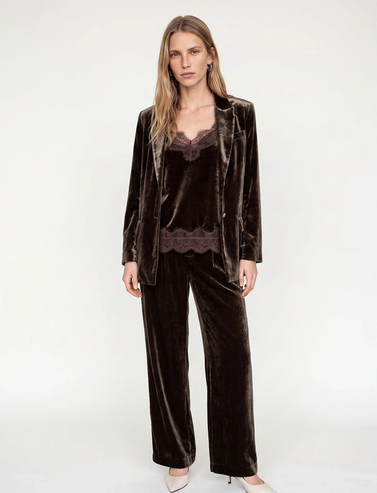 model wearing a brown velvet suit and a brown lace and velvet texture camisole with white heels ona plain grey background