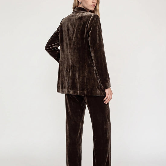 Model wearing a brown velvet suit facing backwards on a plain background