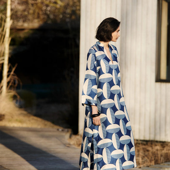 Woman wearing a blue and white patterned kaftan dress from Mondo Corsini standing on a wooden deck.