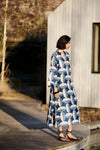 Woman wearing a blue and white patterned kaftan dress from Mondo Corsini standing on a wooden deck.