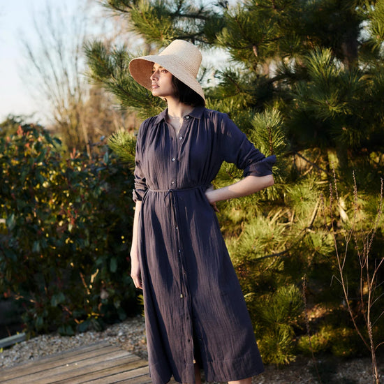 Woman wearing a long dark blue dress by Mondo Corsini with greenery in the background.