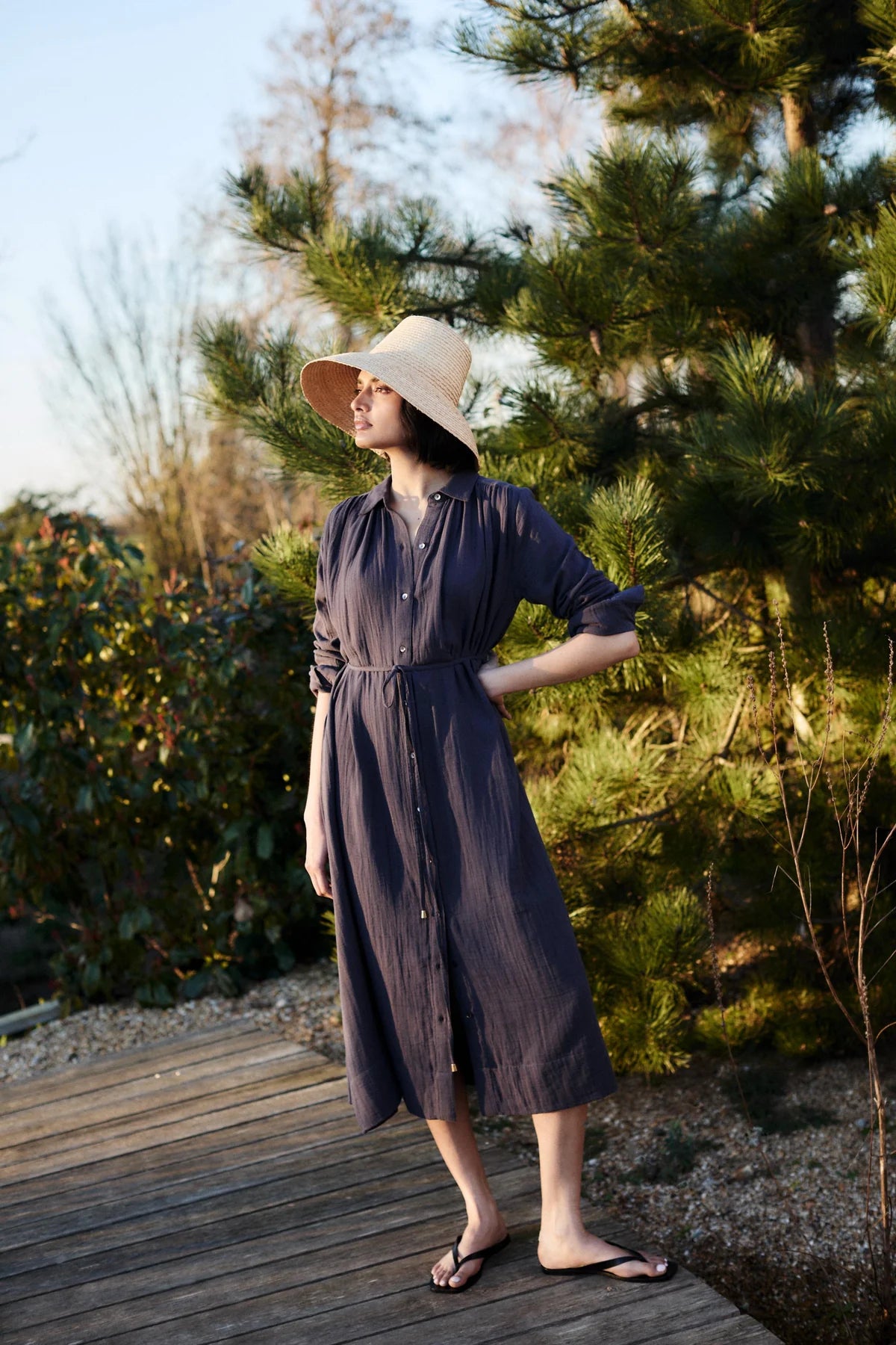 Woman wearing a long dark blue dress by Mondo Corsini with greenery in the background.