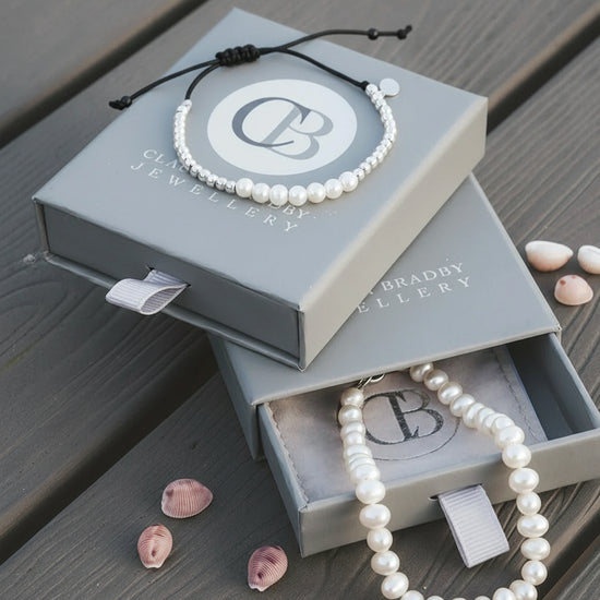 Pearl bracelet on a Clive Bradley Jewellery box with seashells on a wooden surface