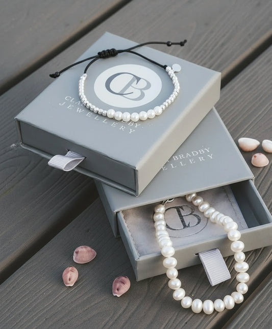 Pearl bracelet on a Clive Bradley Jewellery box with seashells on a wooden surface