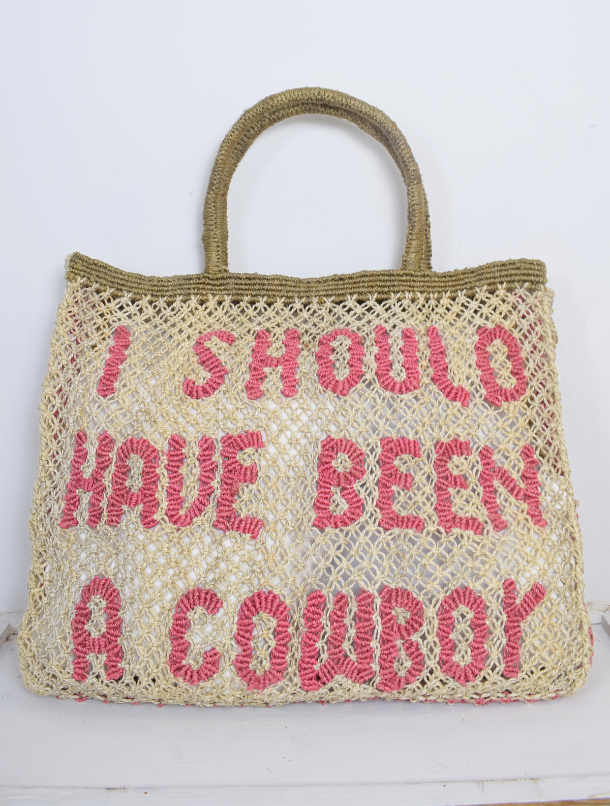 Natural coloured woven bag with pink writing saying 'i should have been a cowboy' 