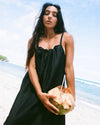 Woman in a black dress holding a coconut on a beach