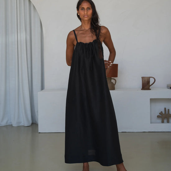 Woman wearing a black slip dress standing in a minimalistic room.