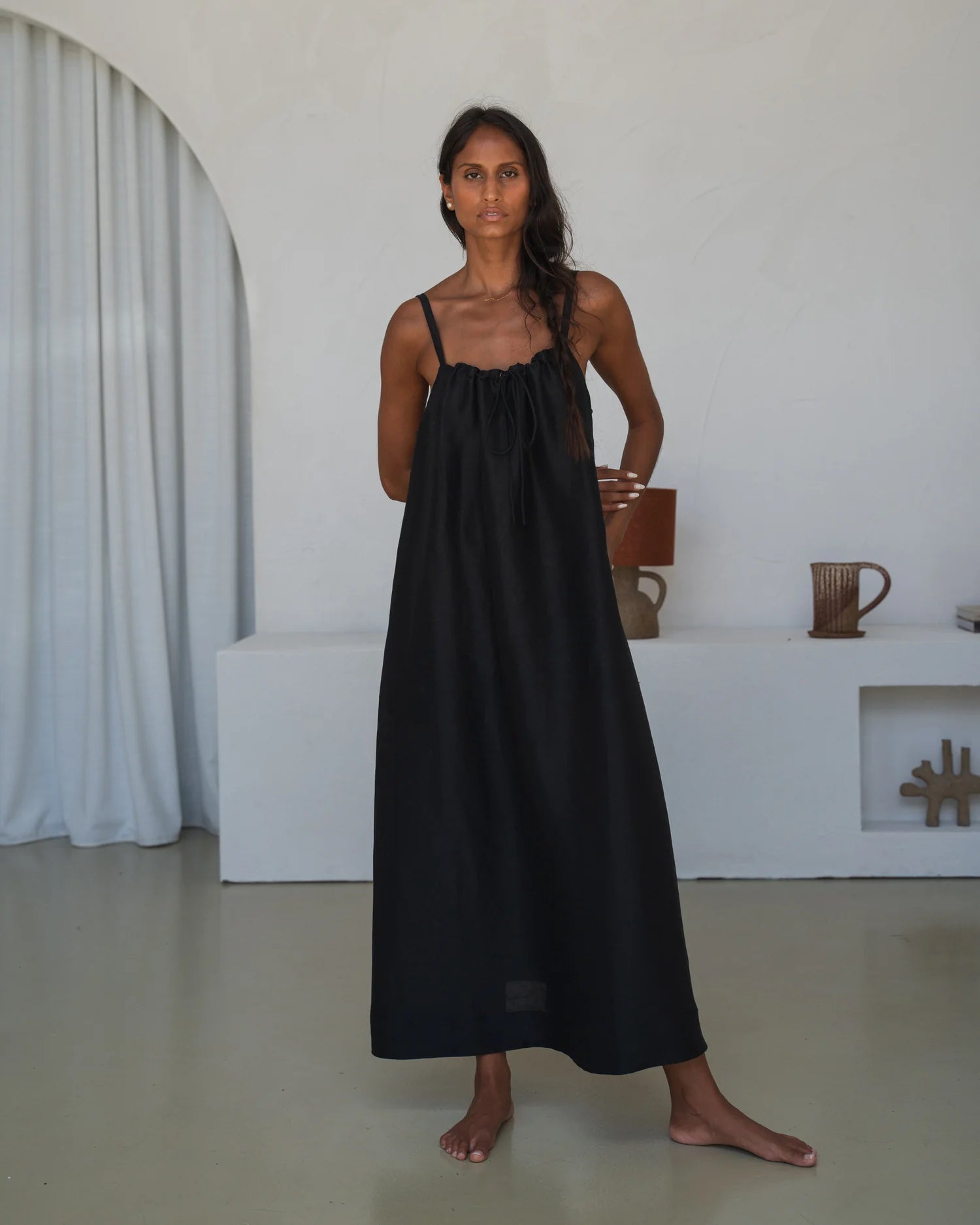 Woman wearing a black slip dress standing in a minimalistic room.