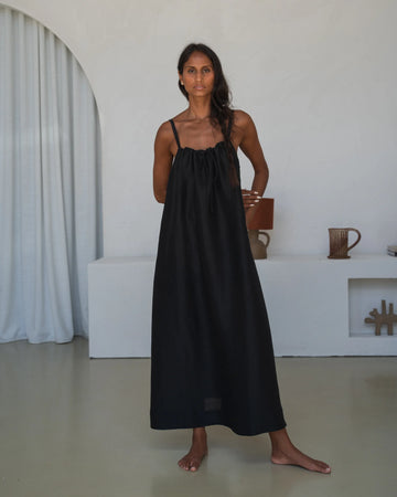 Woman wearing a black slip dress standing in a minimalistic room.