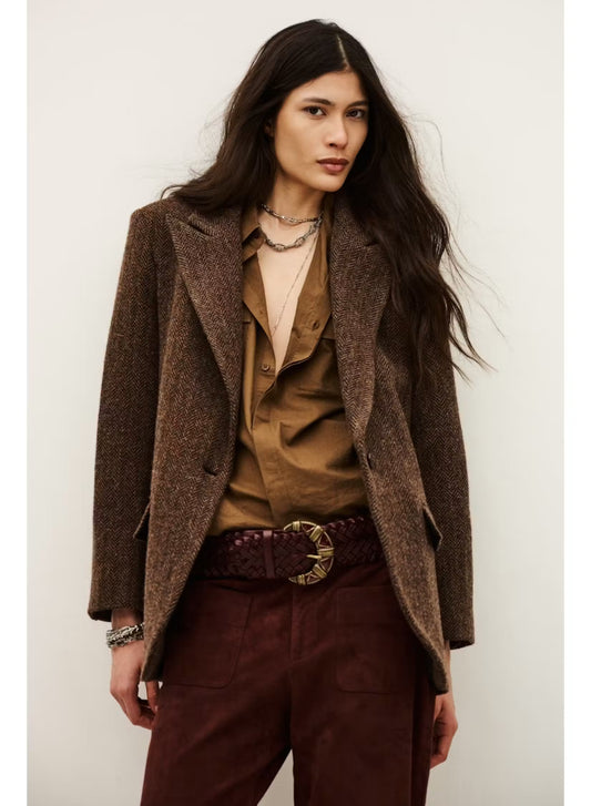 A model wearing a brown textured tweed blazer over a brown button-up shirt, paired with dark burgundy trousers and a dark brown braided belt with a gold buckle, set against a plain off-white background.