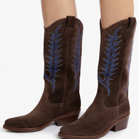 woman wearing Brown cowboy boots with blue embroidery on white background