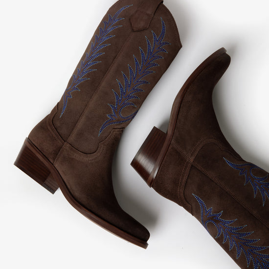 Brown cowboy boot with blue embroidery on white background laying down