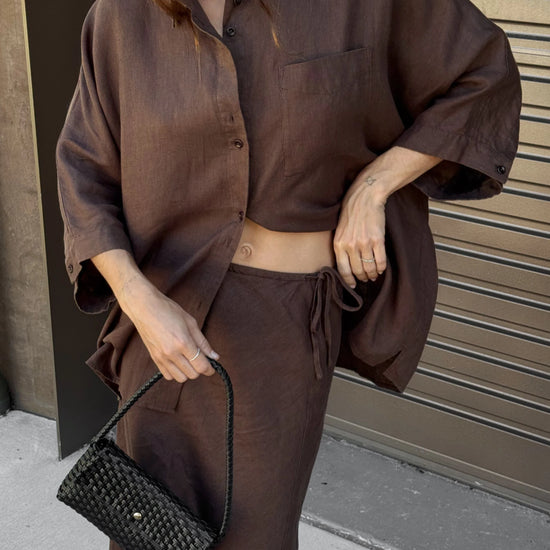 Person wearing a brown outfit holding a black clutch against a neutral background