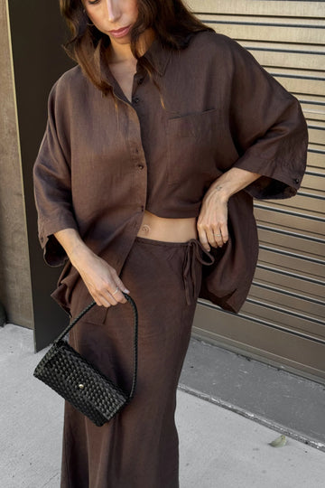 Person wearing a brown outfit holding a black clutch against a neutral background