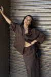 Woman in a brown outfit leaning against a metallic wall.