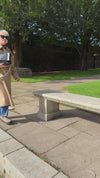 Model video wearing a long camel wool coat walking in shot sitting down and opening black leather handbag.