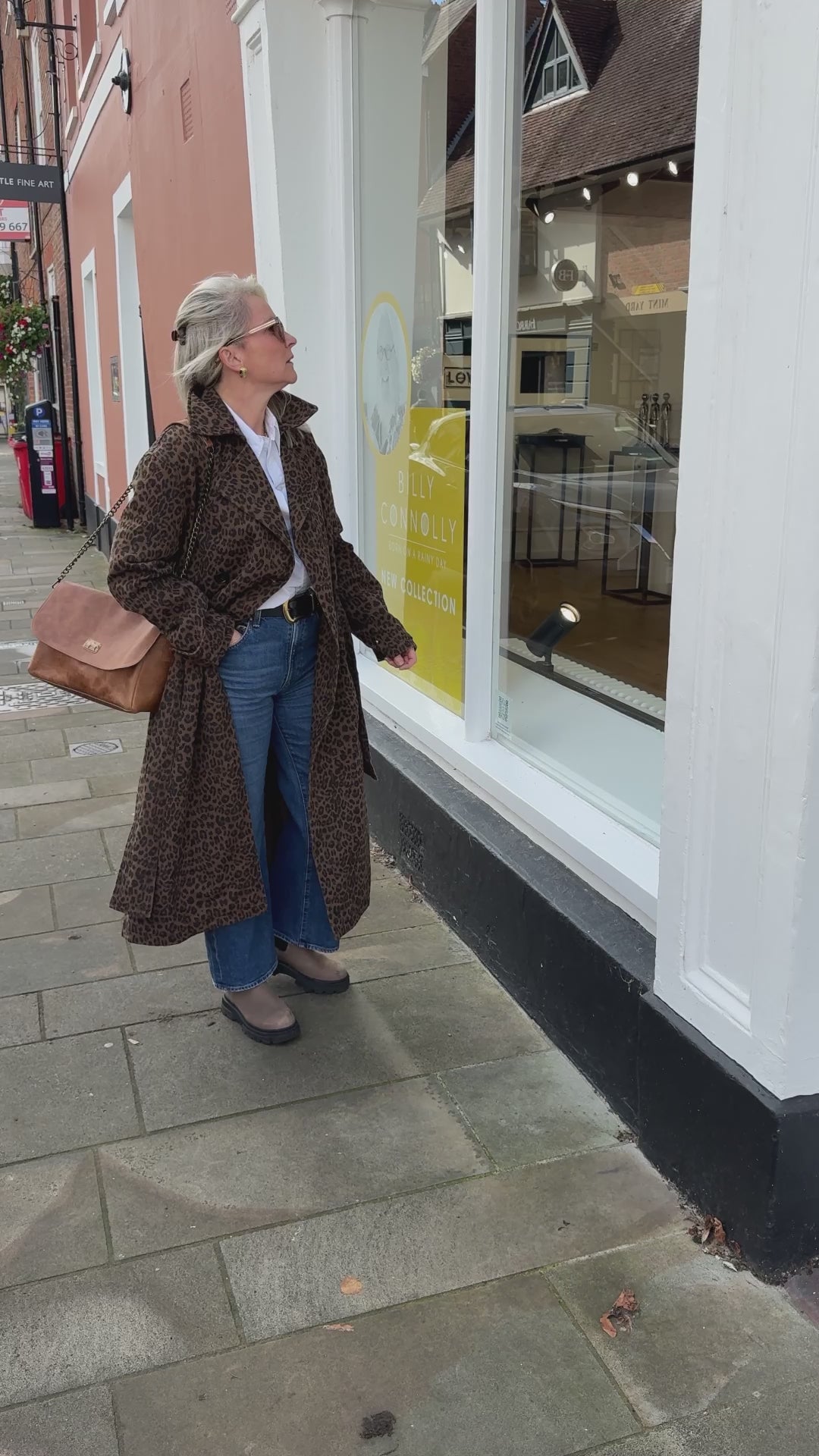 Model video wearing a leopard trench coat and on the shoulder leather caramel handbag with gold detailing.