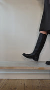 Model wearing tall equestrian style black leather boots shown at different angles. 