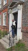 model video stood in doorway wearing faux fur white gilet and crossbody black handbag with circular stamps on the front