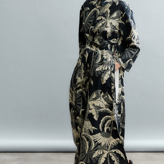 Woman wearing a long, dark patterned coat against a plain background