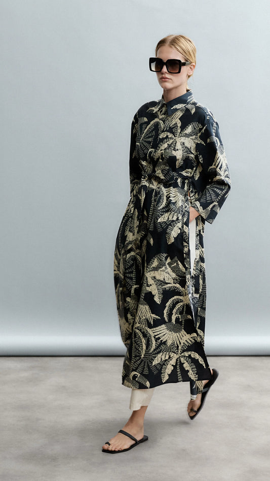 Woman wearing a long, dark patterned coat against a plain background