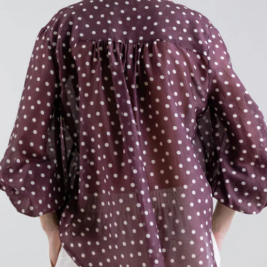 Person wearing a polka dot blouse with a plain background